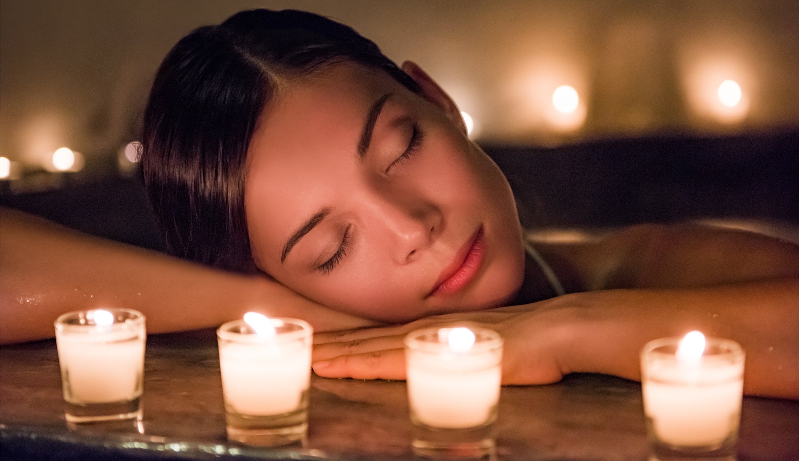 Woman relaxing with her eyes closed surrounded by lit candles