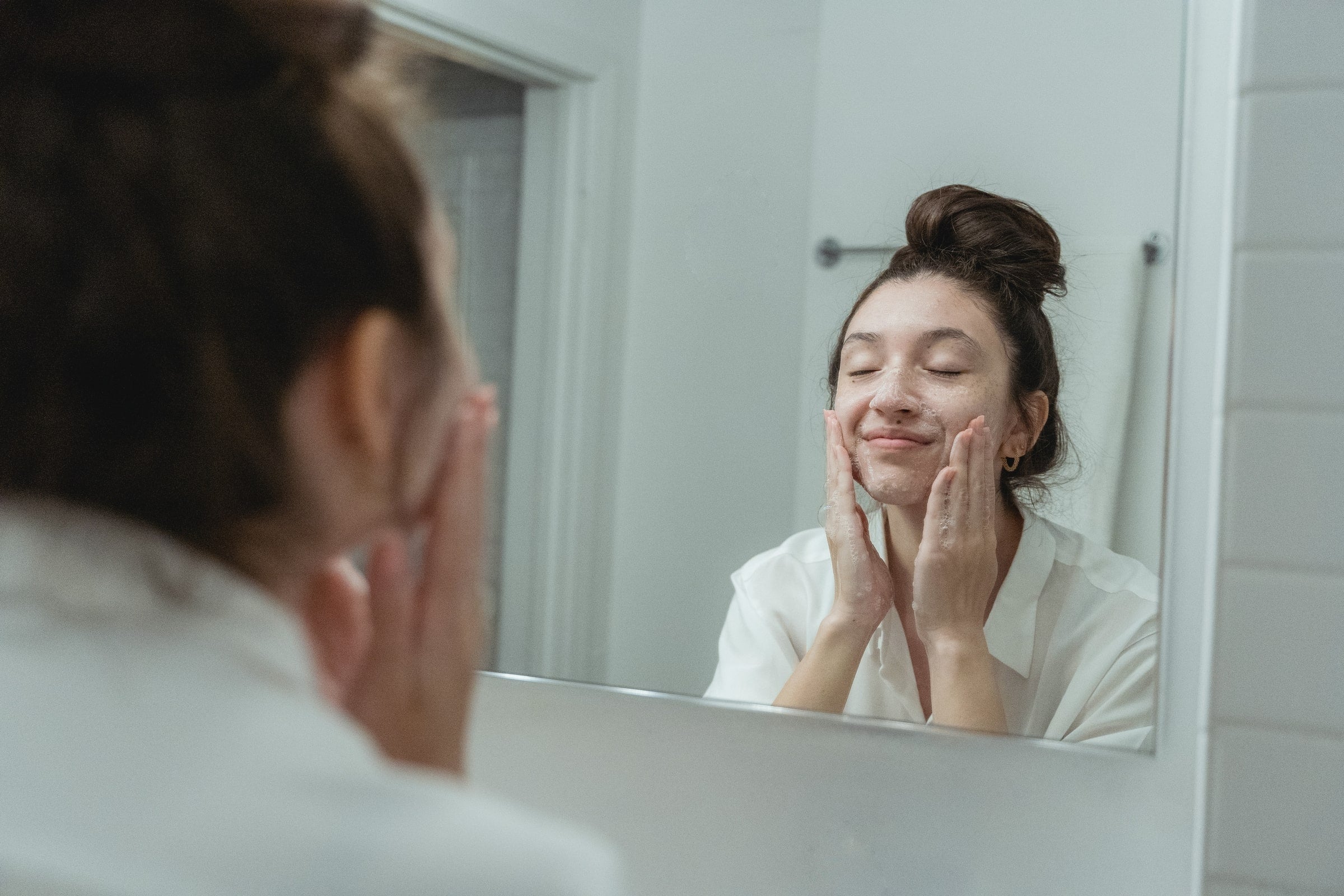 Woman double cleansing her face in the bathroom mirror